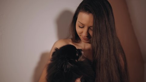 Close view: Funny little spitz dog kissing young nudist woman