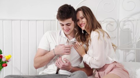 A beautiful couple of young lovers holding a small white kitten sitting in bed. cat breed Nevsky masquerade. pet in a young family.