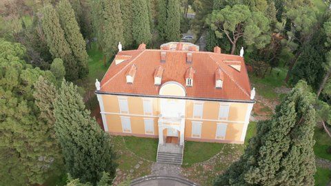 Historical mansion house, surrounded by tall green trees in a park, in Podgorica Montenegro. Exterior of a two story royal palace with red roof, in a garden. Aerial drone view.
