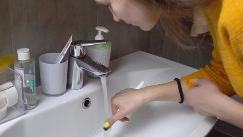 The image of a pretty woman, brushing her teeth, rinsing her mouth with water. The tap is turned on and in front of the sink, she takes a mouthful of water and rinses it, then spits it out.