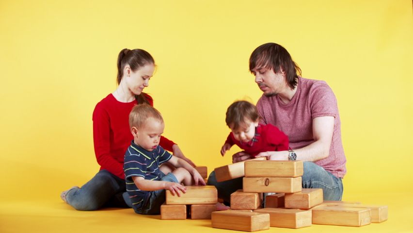 Father and mother are building a tower from wooden blocks with children: 4 years old son and cute little daughter. Studio, yellow background Royalty-Free Stock Footage #1070601097