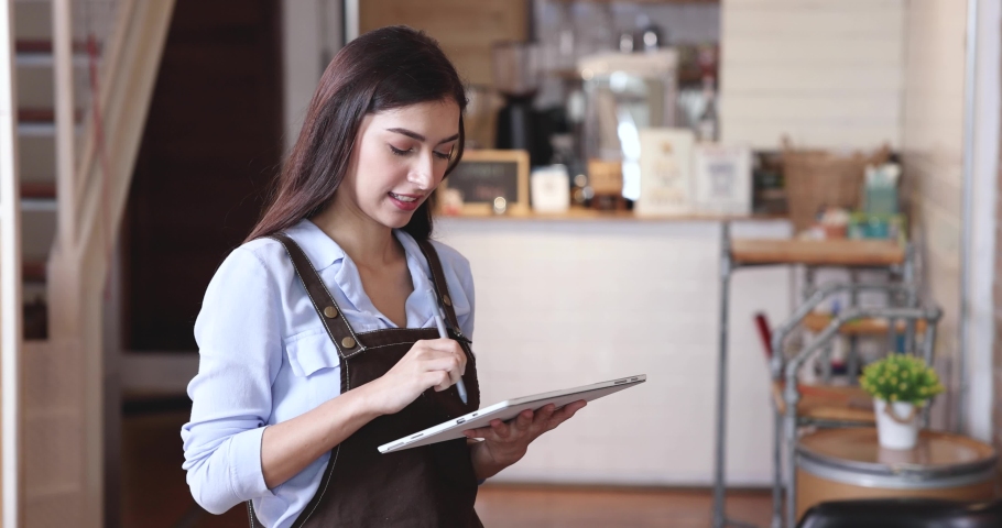 Female coffee shop owner in an apron or a female barista stands in front of the counter, looking at the camera and smiling.