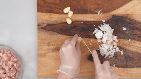 Woman hands wearing gloves peeling garlic on wooden chopping board. Chicken with garlic, paprika, and sour cream step by step recipe, close up video from above