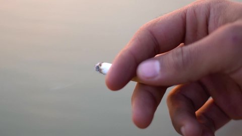 Closeup shot of hand of an Indian man holding burning cigarette. White smoke flying from cigarette in male finger. Lung health issue. 