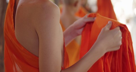Slow motion scene of a Buddhist novice who has just passed ordination in the summer during school holidays is dressing in a yellow robe.