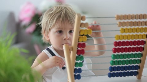 Sweet toddler child, blond boy, learning math at home with colorful abacus, drinking freshly made juice