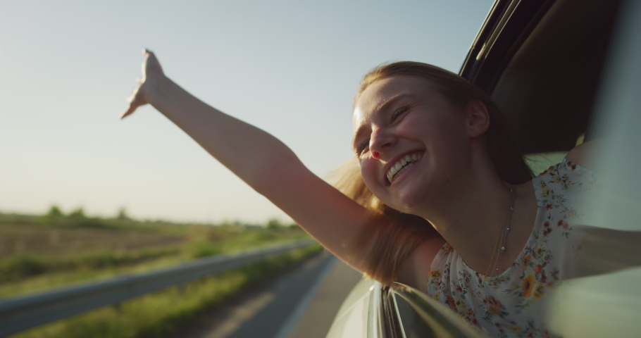 Authentic Shot of an Young Happy Carefree Blonde Hair Woman is Enjoying and Having Fun to Look out the Car Window During a Trip with Friends in a Sunny Day.