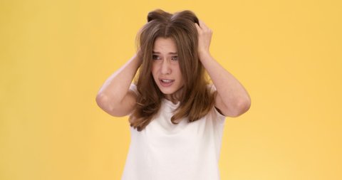 Panic feeling. Young worried woman with mental disorder looking around, grabbing her hair, feeling discomfort, orange studio background, slow motion