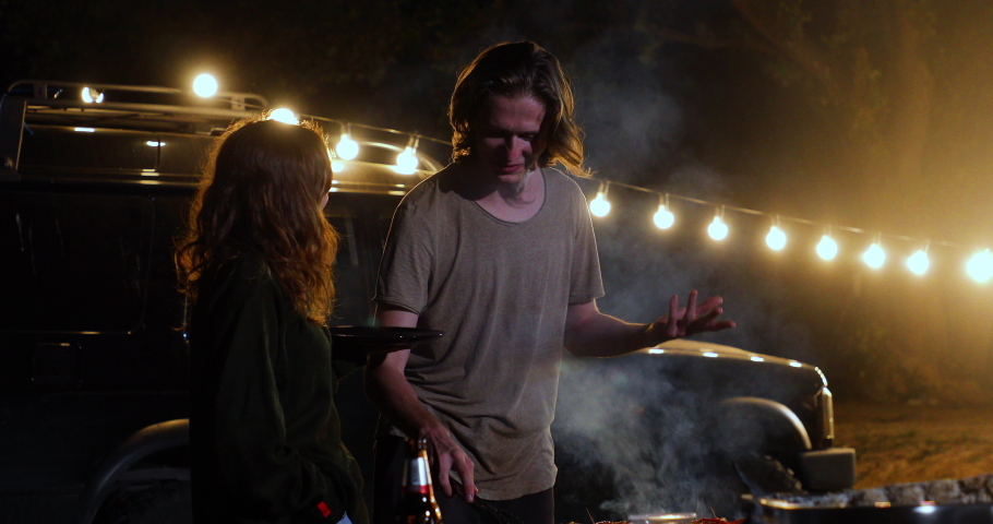 Young caucasian couple making barbecue in dinner party camping at night. 