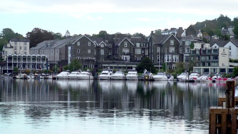 Bowness-on-Windermere marina with motor yachts moored in front of hotels and buildings. Wide shot Lake District, Cumbria, England - a tourist mecca and boating centre.