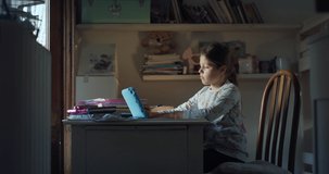 Authentic shot of little girl pupil is writing in notebook at desk while having online lecture with tablet with a teacher in virtual classroom during distance education in her room at home. Covid