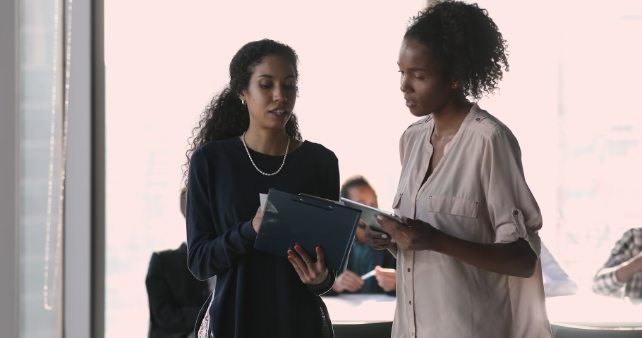 African ethnicity businesswomen walk along office room discussing collaborative project. Mixed-race apprentice asks, specifies details of task, talk to mentor at workspace. Teamwork, mentoring concept | Shutterstock HD Video #1070629951