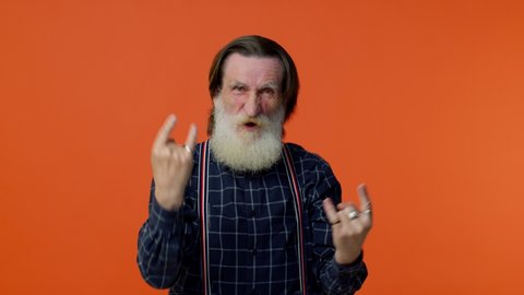 Overjoyed delighted elderly bearded man showing rock n roll gesture by hands, cool sign, shouting yeah with crazy expression, dancing, emotionally rejoicing in success. Senior mature old grandfather