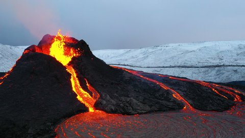 Aerial footage of an icelandic volcano eruptin in 2021 in Reykjanes peninsula, shot at dusk with contrast with snowy mointains and red hot lava 