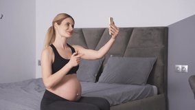 Side view of a beautiful pregnant woman in sportswear, a woman talking on a video link with her spouse