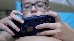 Serious Boy with Glasses Plays Mobile Game on Smartphone in Relaxed State on Bed. Home. Addicted to online video games. Teen entertainment. Concept of technology and Internet addiction. Close-Up. 4K.