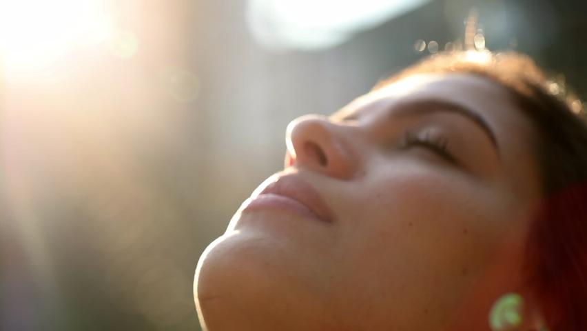 Contemplative young woman looking up to sky with faith and hope. Faithful girl profile face with lens-flare outside