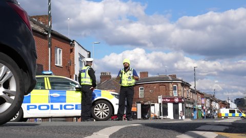 SALFORD, MANCHESTER, UNITED KINGDOM - APRIL, 12, 2021: Low angle view of police roadblock. Two police officers standing by their car and diverting traffic around closed part of Liverpool Road.
