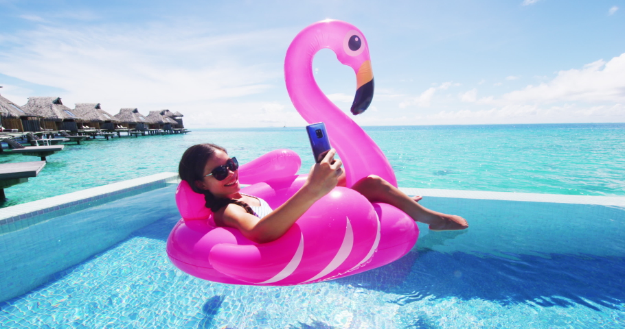 Phone - Travel vacation woman on inflatable Flamingo float mattress using app on mobile cell phone in swimming pool, maybe for booking hotel while relaxing sunbathing on resort pool in bikini Royalty-Free Stock Footage #1070645476