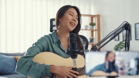 Teenage Asia girl influencer play guitar music use microphone record with smartphone for online audience listen at home. Female podcaster make audio podcast from her home studio, Stay at home concept.