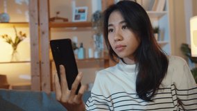 Sick young Asian lady hold medicine sit on couch video call with phone consult with doctor at home night. Girl take medicine after doctor order, quarantine at house, Social distance corona virus.