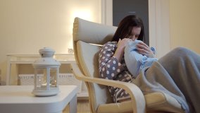 Mother with baby in her arms sits in a chair in living room at home, modern apartment in the evening. High quality 4k footage