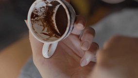 A woman's hand is telling about coffee fortune telling.A woman's hand holding a coffee mug with coffee grounds is looking at coffee fortune telling.Shoot from the shoulder.Video for the vertical story
