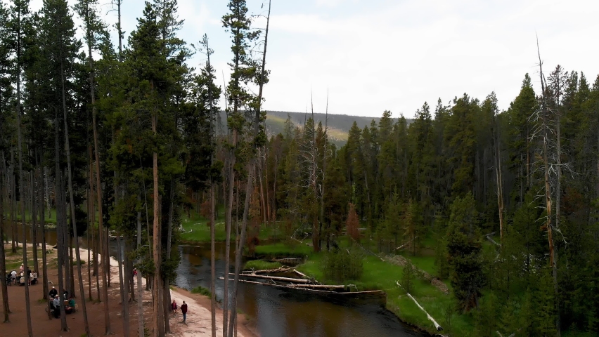 Slow downward aerial tilt above a large river and picnic area among the trees near Yellowstone in Wyoming.