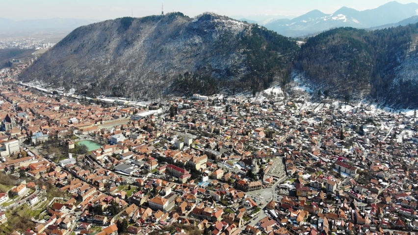 Aerial shot of historic city center of Brasov and Carpathian mountains in the background on a sunny winter day