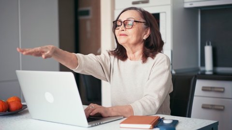 A happy mature older woman finishing her workday at home. Smiling 60s middle-aged businesswoman closes a laptop, takes off her glasses, and reclining in a chair.