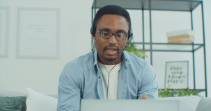 Young afro american man in glasses and headphones holding video call consultation with mentor, studying remotely at home. Businessman discussing project ideas with colleagues distantly.