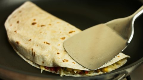 Frying a freshly wraped chicken quesadilla on a frying pan. Process of making mexican quesadillas