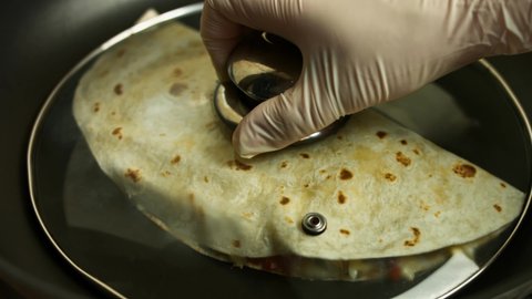 Frying a freshly wraped chicken quesadilla on a frying pan. Covering the quesadilla. Process of making mexican quesadillas