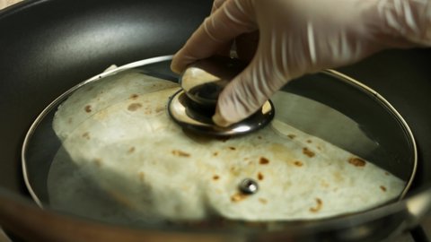 Frying a freshly wraped chicken quesadilla on a frying pan. Taking off the cover. Process of making mexican quesadillas