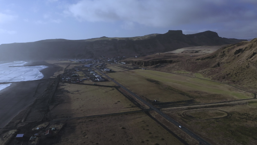 Seafront Village Of Vik At Black Sand Beach With Rock Mountainscape In Background At South Iceland. - Aerial Drone Shot
