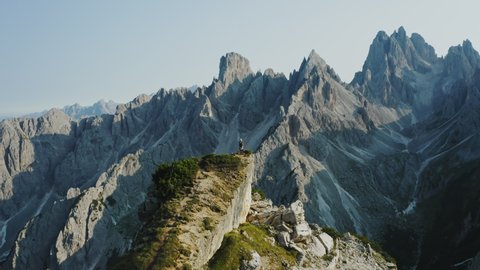 Women staying on cliff edge in front of Cadini di Misurina mountains group in Dolomites, Italy. Part of Tre Cime di Levaredo national park and UNESCO world heritage site. Aerial drone orbit footage