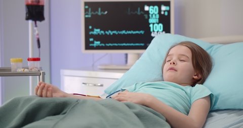 Sick little girl sleeping in bed having blood transfusion in hospital. Portrait of sick kid patient lying unconscious in hospital bed having blood transfusion procedure