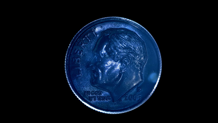 On a black background, one dime coin is glitters in the rays of light. Macro. Closeup