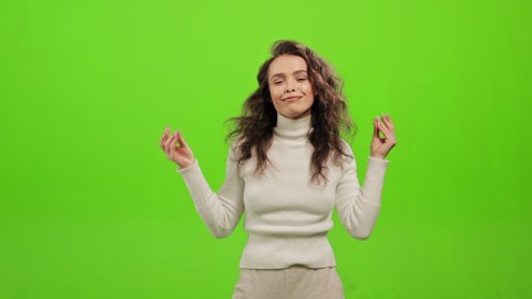 The woman is standing and looking at the camera. She is snapping her fingers and dancing. She is smiling. She is standing on a green background. Green screen. 4K