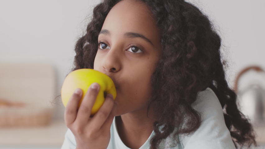 Healthy diet. Close up portrait of happy black girl biting and eating ripe green apple, looking at camera at kitchen interior, slow motion | Shutterstock HD Video #1070685808