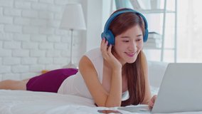 Happiness Asian young woman wear earphone lying on bed relax with music sing a song at home,Recreation young girl chilling with music in cozy bedroom