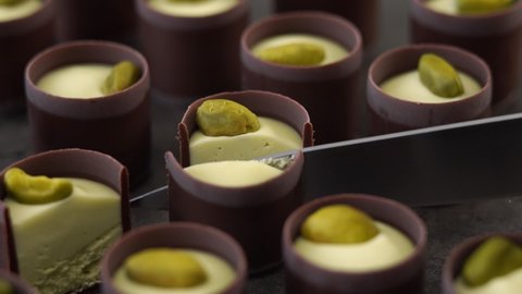 Close up of knife cuts milk chocolate candie with creamy filling and pistachio nuts. Food dessert background. Pastry shop concept