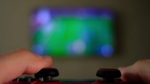Close view of a gamer's hands playing soccer (football, fifa) simulator video game on console using joystick. 