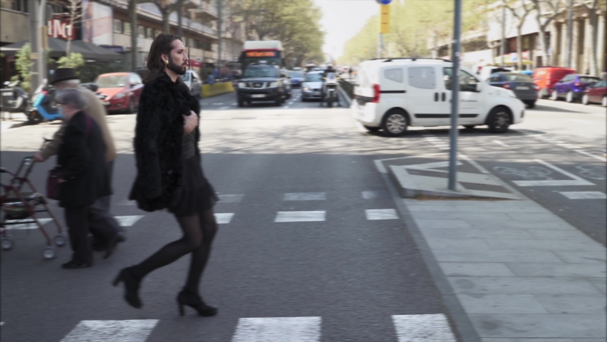 Drag queen with beard, dark dress skirt and high heeled boots croossing a street in a big city. Respect, sexual equality, diversity and pride for lgbt people