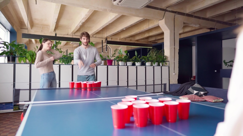 Group of young people playing beer pong in a large room