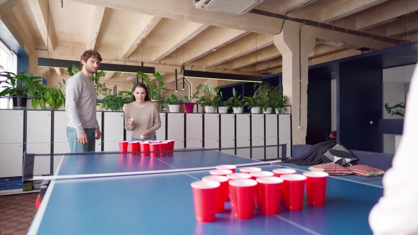Group of young people playing beer pong in a large room