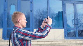 Young caucasian blond man in a plaid blue red shirt is taking a panorama picture on a smartphone. The concept of mobile photography, video, smartphone use in life.