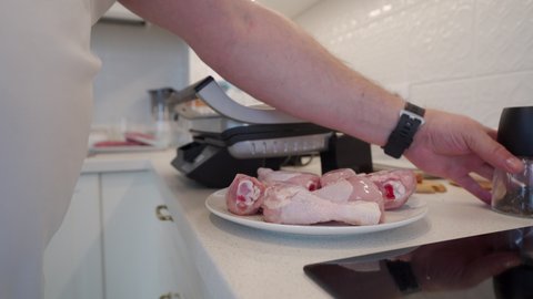 Man preparing food in the kitchen cooking chicken drumsticks in electric grill sprinkling with ground pepper, using pepper mill. High quality 4k footage