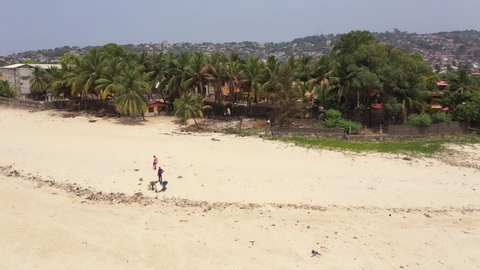 FREETOWN, SIERRA LEONE -3 FEB 2021: Aerial boys on beach picking up trash Freetown Sierra Leone. Coast of west Africa extreme poverty and hunger. Tropical climate environment. Pollution trash.