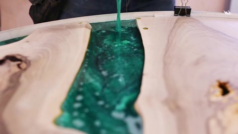 Process making of a craft resin and wood table. Liquid epoxy is poured into a mold with wooden blanks.	